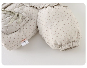 Gros plan de la veste matelassée bébé à fleurs avec volants aux poignets et cordons