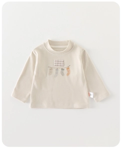 Détail du t-shirt bébé crème à manches longues avec écusson à carreaux et étiquette taille 73