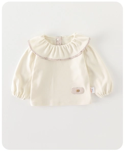 Close-up of baby cream long sleeve shirt with ruffle collar and decorative patch