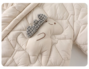 Détail d'un body matelassé pour bébé avec un écusson dinosaure 3D et motif hexagonal