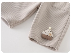 Détail d'un pantalon en maille gaufrée pour bébé beige avec écusson champignon 3D et bouton