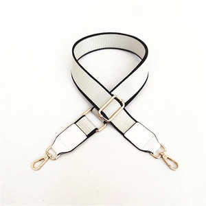 Detail of adjustable off-white woven bag strap with black edges and gold metal hardware
