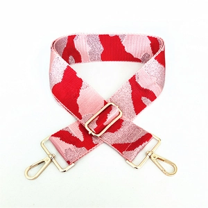 Detail of red and pink camo pattern fabric bag strap with golden metal carabiner hooks