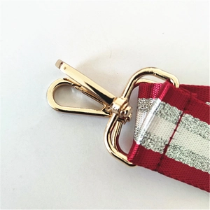 Close-up of golden metal swivel hook with red and white striped woven bag strap