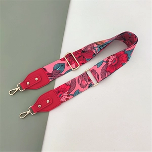 Detail view of pink wide canvas bag strap with red floral pattern and golden metal buckles