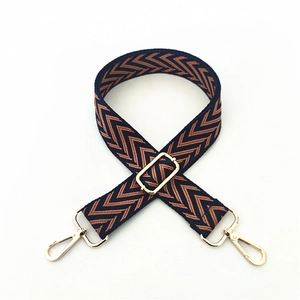 Detail of adjustable wide woven bag strap with brown herringbone pattern and gold metal hooks