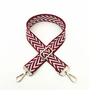 Detail of adjustable woven red and white zigzag bag strap with golden metal swivel hooks