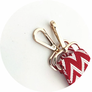 Macro detail of red and white woven shoulder strap with gold metal lobster clasps