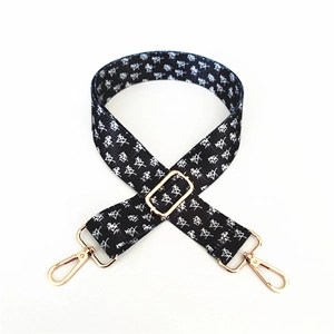 Detail of adjustable black woven bag strap with white pattern and golden metal buckles