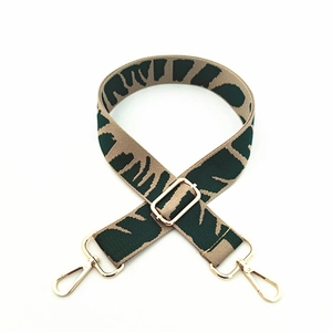 Detail view of durable woven shoulder strap with green leaf pattern and gold metal hooks