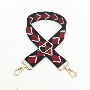 Detail of adjustable canvas bag strap with red and black argyle pattern and gold hooks