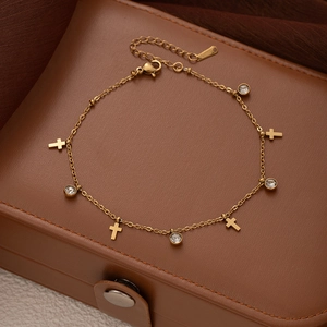 Detail of gold titanium steel anklet with cross charms and zircons on leather
