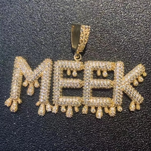 Macro view of gold-plated MEEK pendant with cubic zirconia dripping letter design