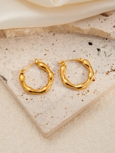 Detail of irregular wave-shaped gold stainless steel earrings on a beige stone surface