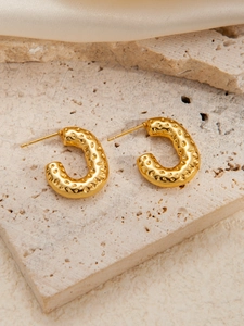 Macro view of gold-tone stainless steel C-shape earrings with hammered texture
