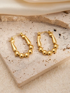 Detailed close-up of golden U-shaped bead earrings on a textured stone and silk surface