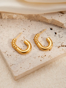 Detailed macro view of gold C-shaped earrings with mixed smooth and spiral texture