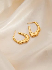 Makroaufnahme goldener Edelstahl-Ohrringe im Lava-Stil auf cremefarbenem Seidenstoff