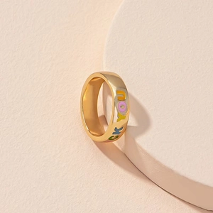 Golden flower ring with colorful FUCK YOU enamel letters on a minimalist display stand