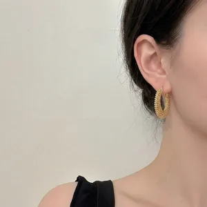 Elegant gold woven beaded hoop earrings with textured finish on a female model