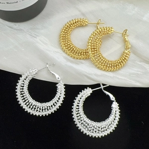 Macro detail of gold and silver textured hoop earrings with woven bead metal surface