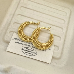 Detailed view of gold beaded hoop earrings with intricate metallic texture on beige tray