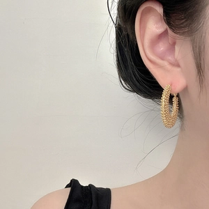 Detailed macro view of gold-tone woven beaded texture hoop earrings on model