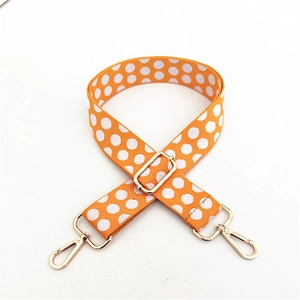 Macro detail of adjustable woven bag strap with orange and white polka dots and gold hardware