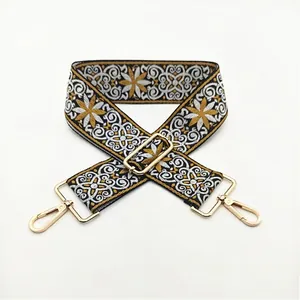 Close-up of ethnic embroidered bag strap with gold metal buckles on a white background
