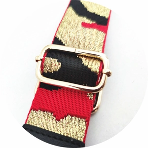Detail of red and black camouflage bag strap with gold metal buckle and woven texture