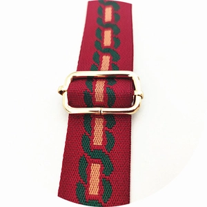 Close-up of adjustable red and green woven handbag strap with gold metal buckle hardware