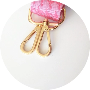 Close-up of pink houndstooth bag strap featuring golden metallic lobster clasps and weaving