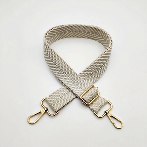Close-up of adjustable beige herringbone woven bag strap with gold metal buckles