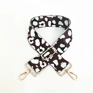 Detail of adjustable leopard print bag strap with golden metal clasps on white background