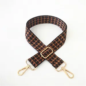 Detail of adjustable wide shoulder strap featuring classic brown houndstooth pattern and gold hooks