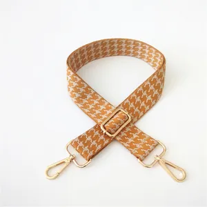 Detail of orange and beige houndstooth adjustable guitar style bag strap with gold clips