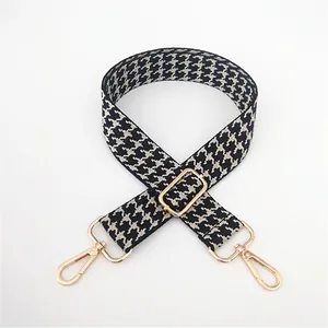 Adjustable black and white houndstooth bag strap with gold metal hooks and buckle