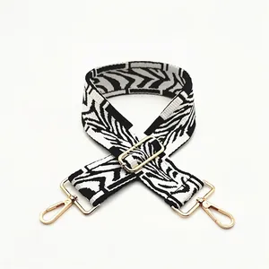 Detail of adjustable black and white geometric pattern wide bag strap with gold metal hooks
