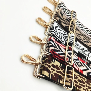 Close-up of wide woven bag straps with colorful ethnic patterns and gold metal hooks