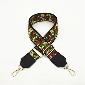 Detail of embroidered floral bag strap with green base, PU leather ends, and gold metal hooks