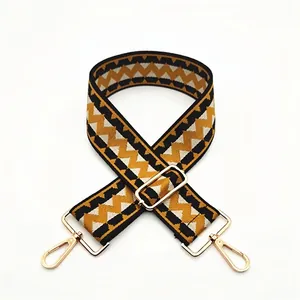 Close-up of wide woven bag strap with golden metal lobster clasps and geometric pattern