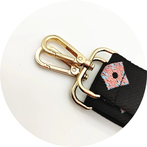 Close-up of golden swivel hook with pink and blue geometric embroidery on black strap