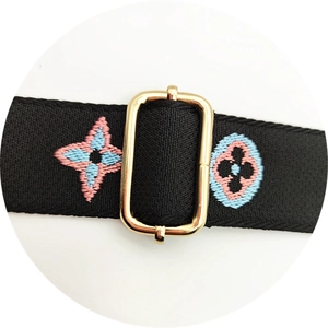 Detail of black adjustable handbag strap with clover embroidery and gold metal buckle