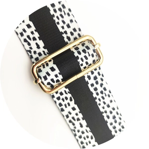 Detail of adjustable wide bag strap with black and white spotted pattern and gold buckle