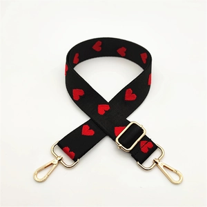Close-up of black bag strap with red heart patterns and golden metal swivel hooks