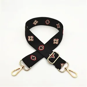 Close-up of black wide jacquard bag strap with red floral pattern and gold metal hooks