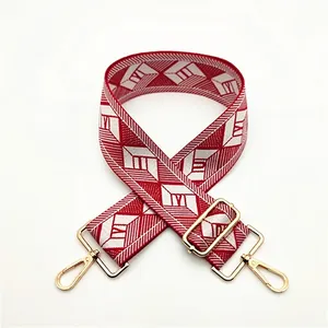 Detail of red and white geometric jacquard bag strap with adjustable gold metal buckle