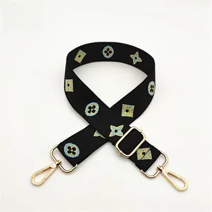 Detail view of adjustable black embroidered bag strap with blue gold clover and gold hooks