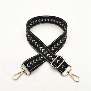 Macro detail of black and white V-pattern woven bag strap with gold metal hooks