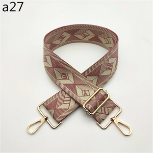 Detail of wide fabric bag strap with pink geometric pattern and gold hardware